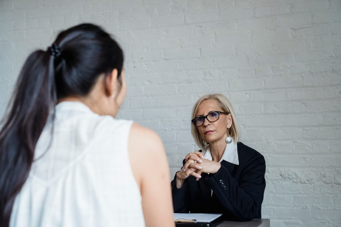 Two people talking across a table in a plain, quiet room.